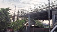 Kabel internet terpasang pada tiang listrik PLN di kawasan permukiman.