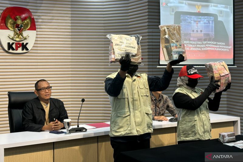 Pelaksana Tugas (Plt.) Direktur Penyidikan Komisi Pemberantasan Korupsi Achmad Taufik Husein (kiri) mempersilakan dua petugas menunjukkan barang bukti kasus dugaan korupsi dalam penerimaan mahasiswa baru Universitas Jenderal Soedirman (Unsoed), di Gedung Merah Putih KPK, Jakarta, Jumat (21/8/2026). ANTARA/Rio Feisal
